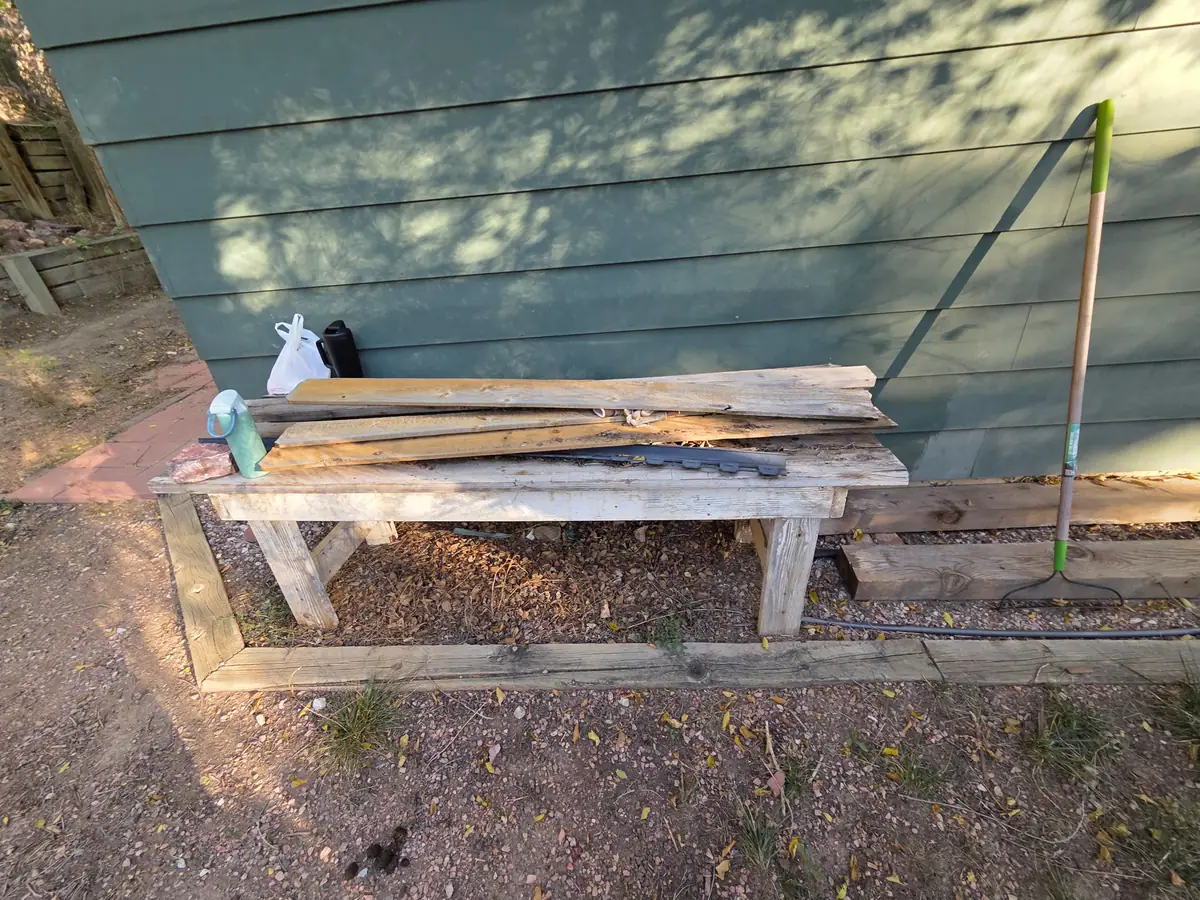 A wooden bench stacked with boards against the house siding