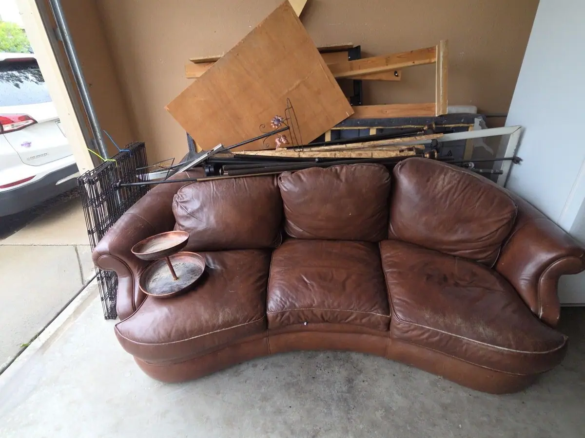 A leather couch and broken furniture left in a garage
