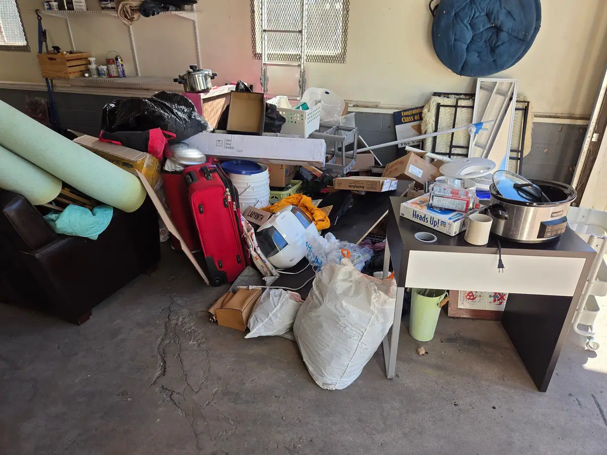 A garage packed with boxes bags a chair and a desk