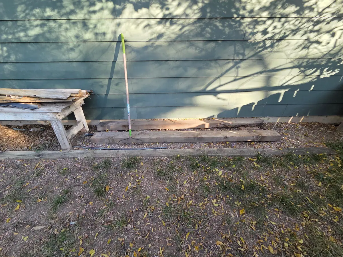 Lumber and a bench lying in a garden bed along the house