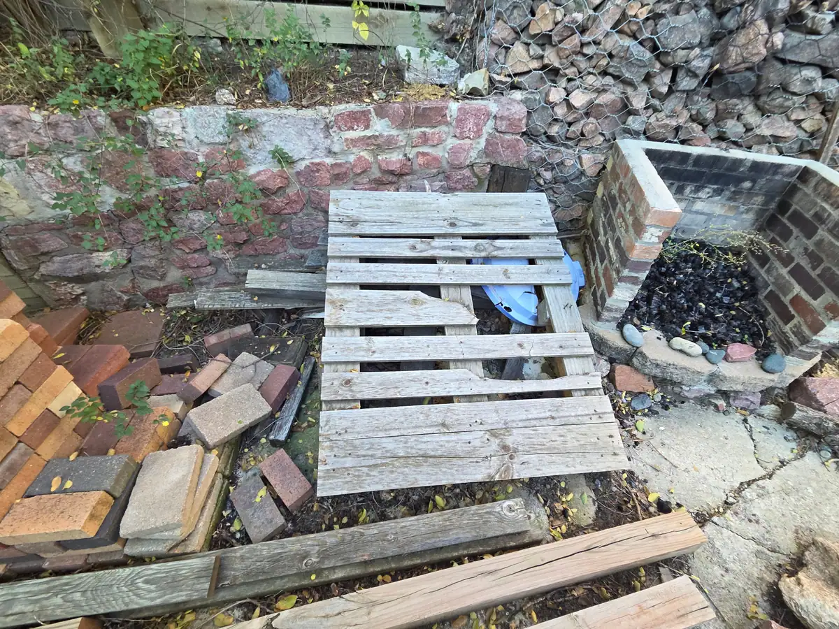 A pallet with loose bricks and boards beside a brick wall