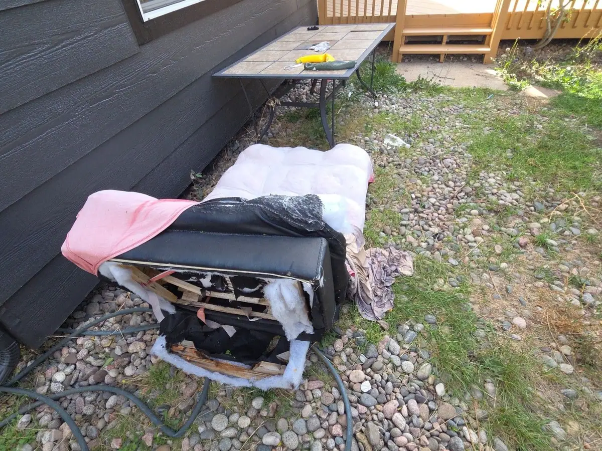 An old mattress and household junk along the side of a house