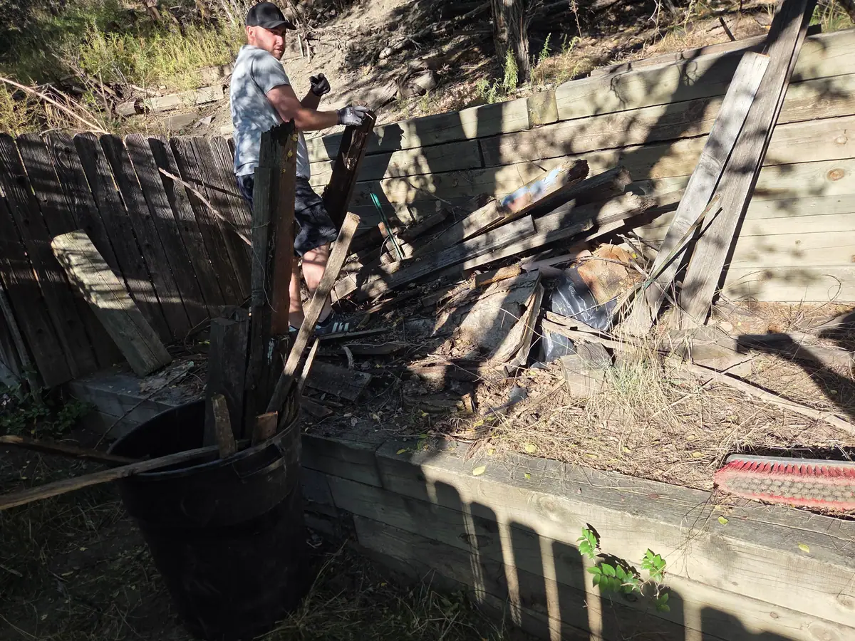 Broken fence boards and timbers piled against a retaining wall