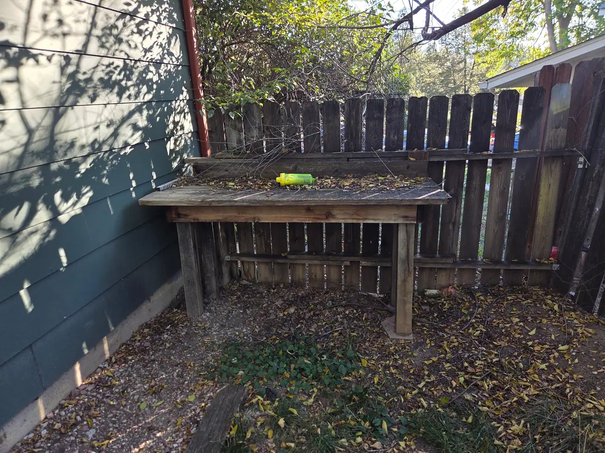 An old wooden workbench and leaves in a fenced corner