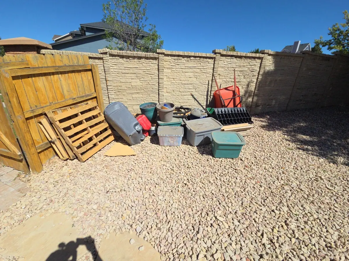 Old pallets and storage bins and yard clutter piled against a block wall