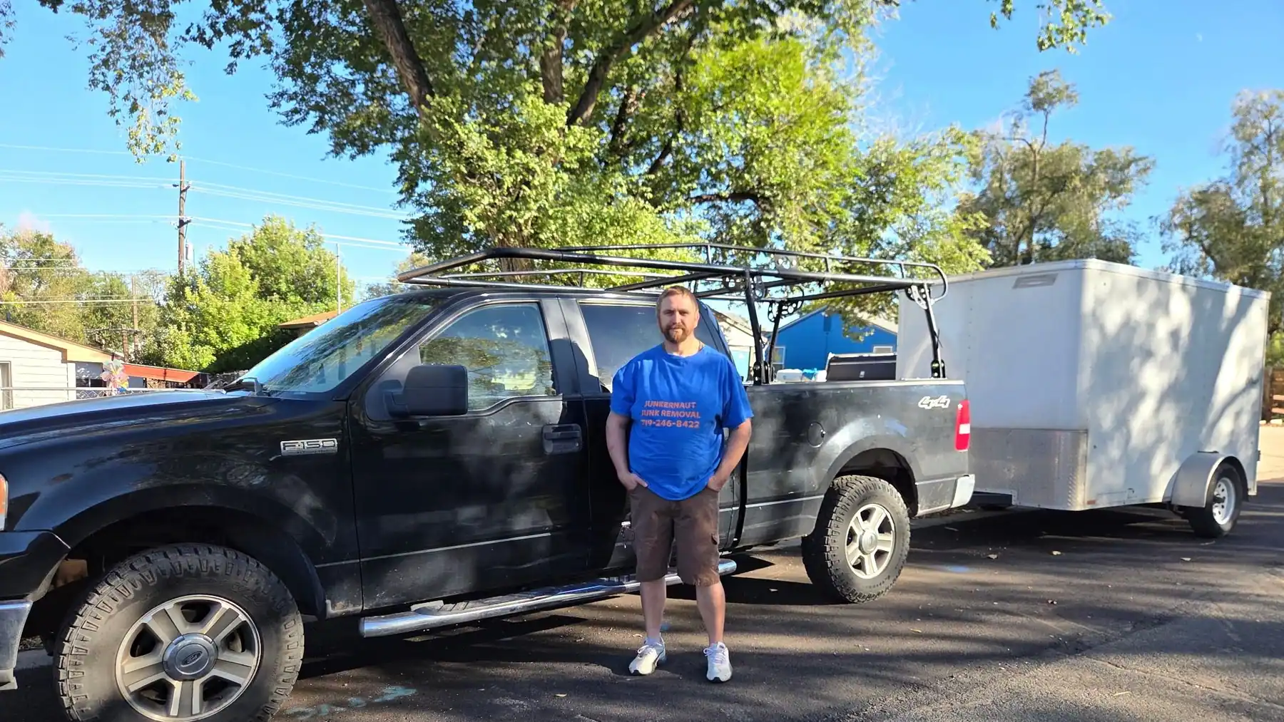Justin in his Junkernaut shirt beside his F-150 with the white cargo trailer hitched behind
