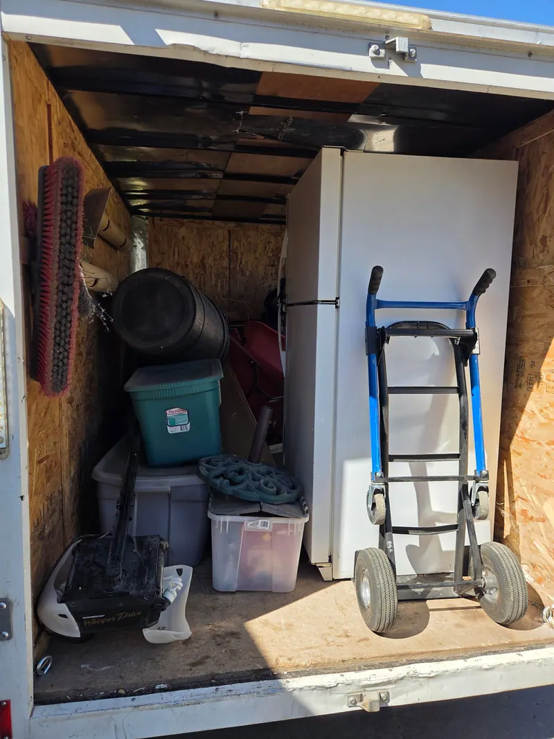 A refrigerator and storage bins loaded in the cargo trailer with a hand truck