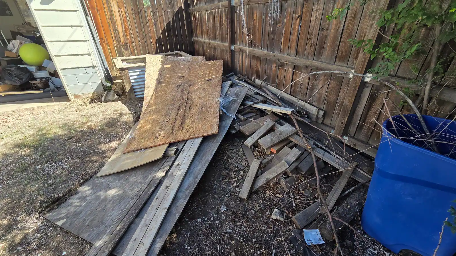 Old boards plywood and scrap wood piled along a backyard fence