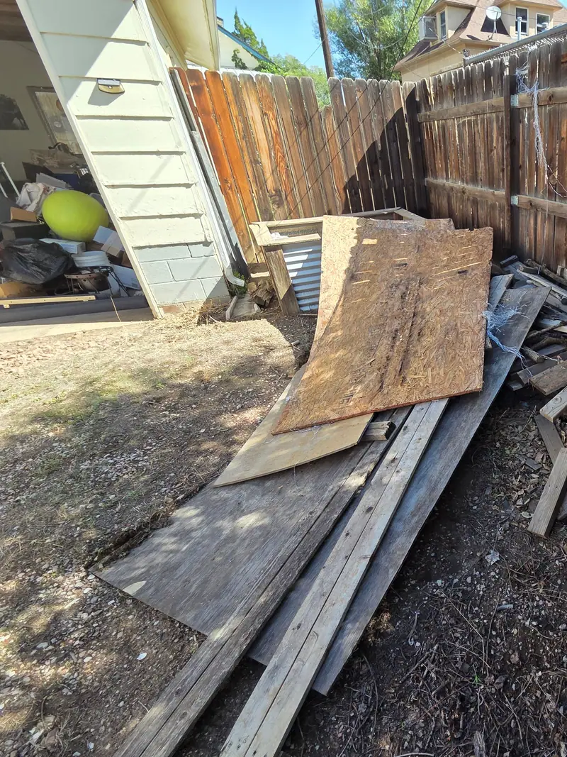 Old boards plywood and scrap wood piled along a backyard fence