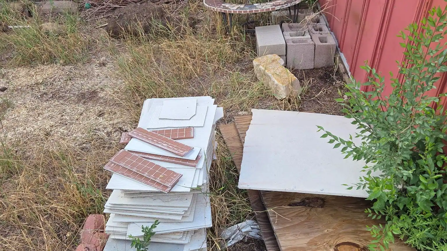 Old tiles and bricks and plywood piled beside a red shed