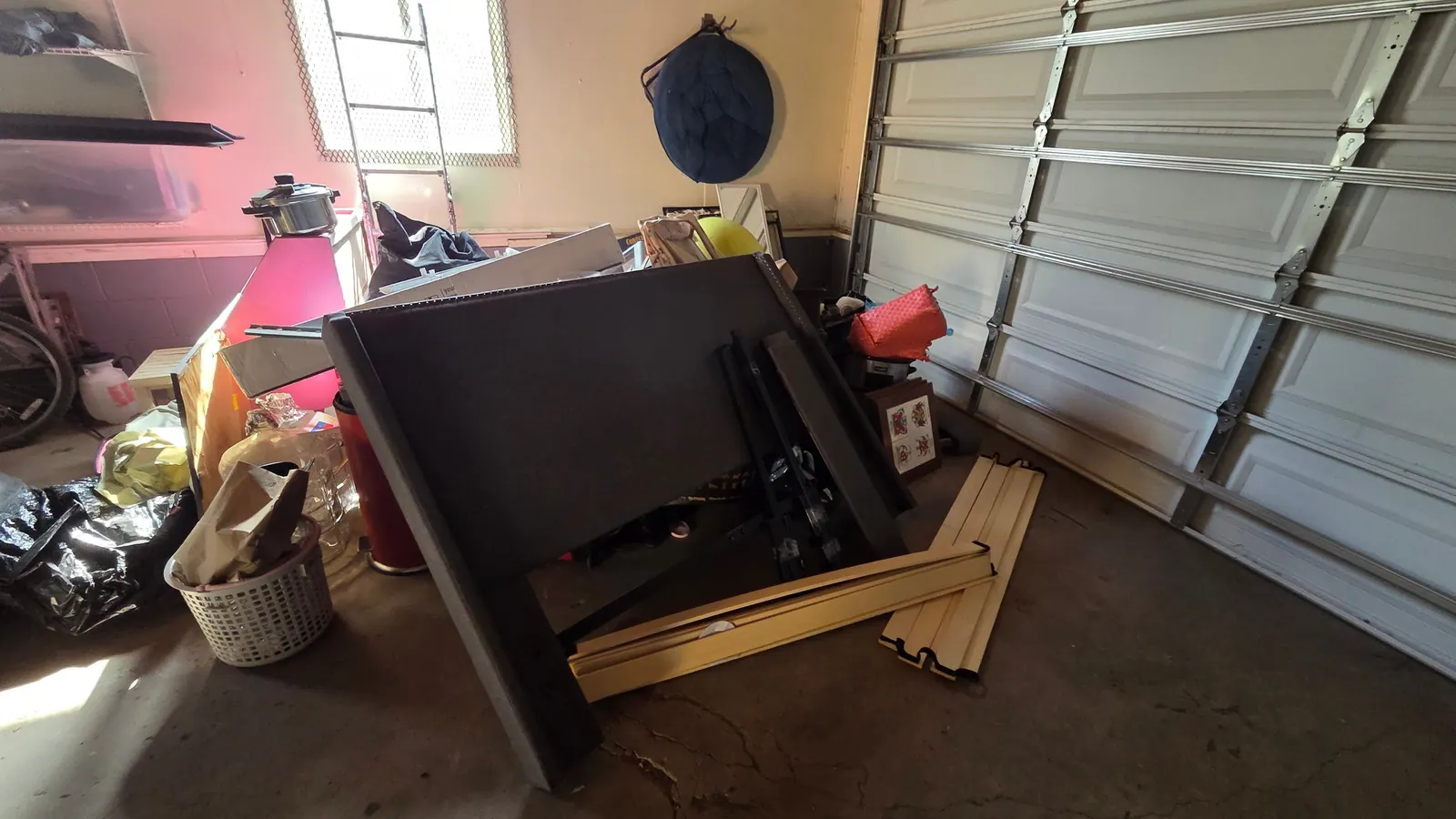 A broken bed frame and household junk piled inside a garage