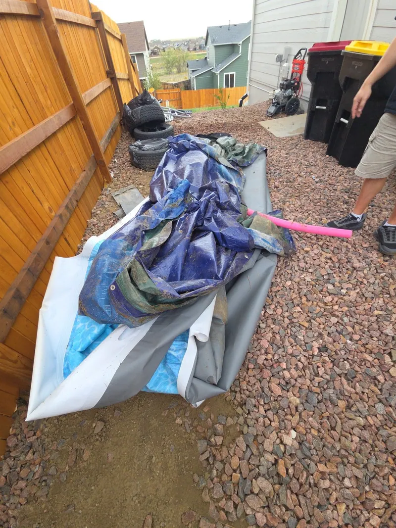 Tarps and an old pool float piled along a side fence